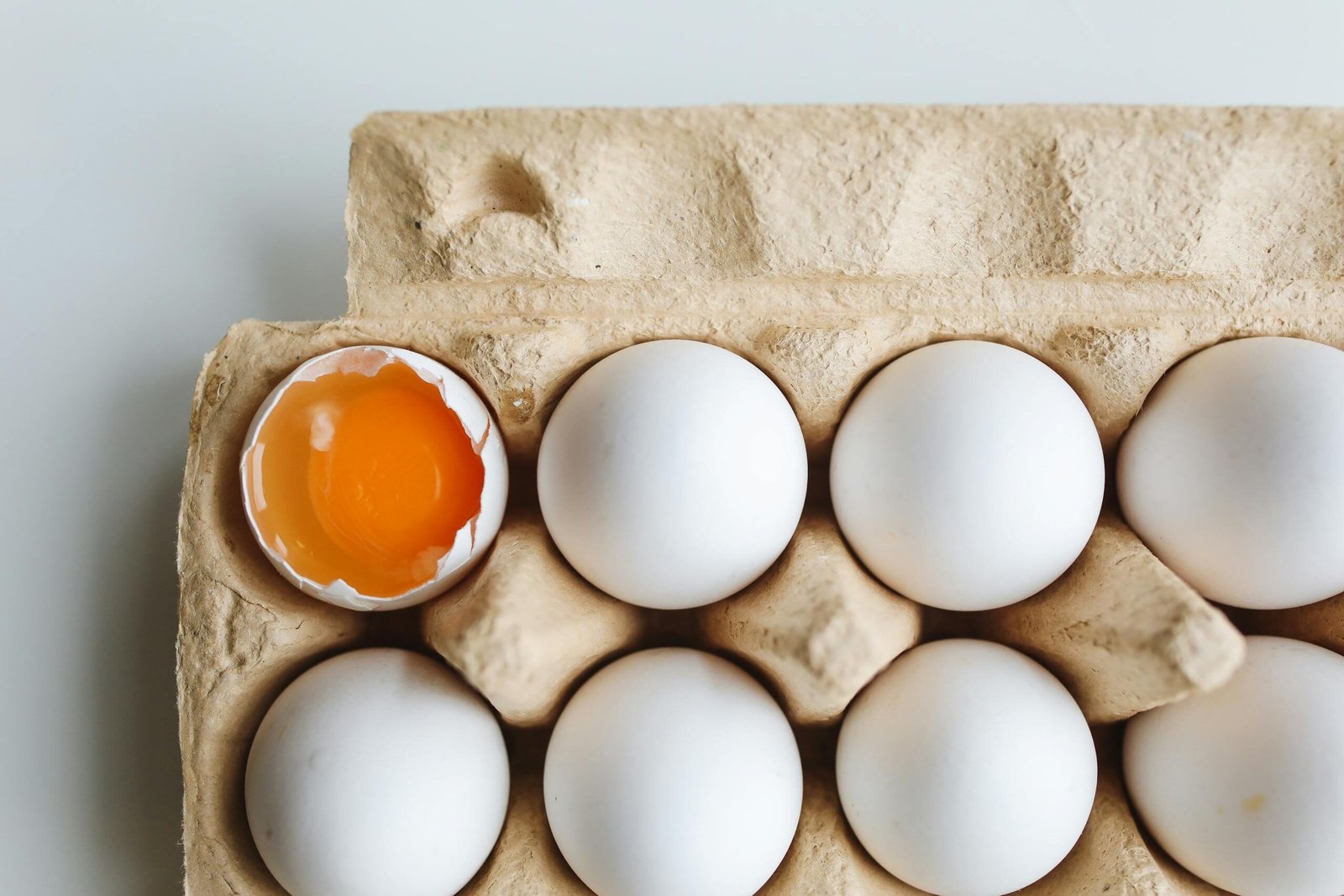 A carton of white eggs with one cracked, revealing vibrant yolk. Ideal for food and health themes.