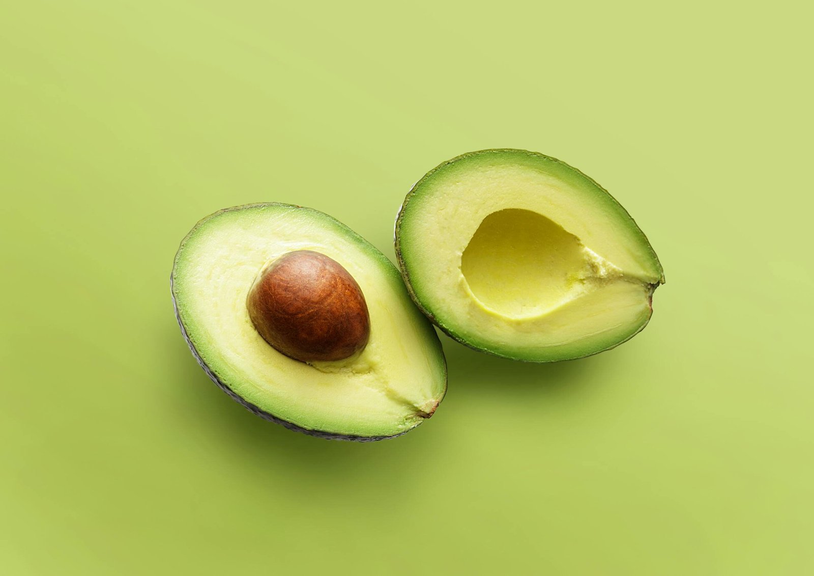 Close-up of fresh avocado halves on a vibrant green backdrop, showcasing its ripe texture.